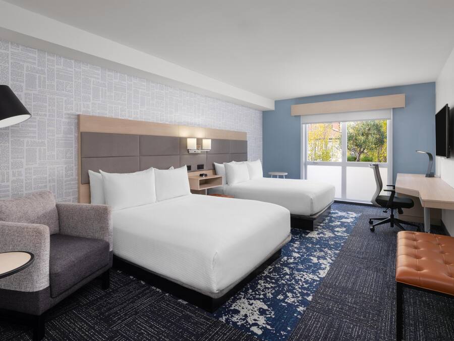 Una habitación de hotel con dos camas, un escritorio, una silla, un sofá y una lámpara.