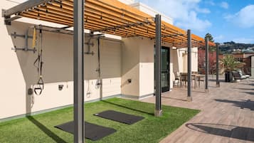 An outdoor workout area with exercise equipment, artificial grass, and a pergola structure.