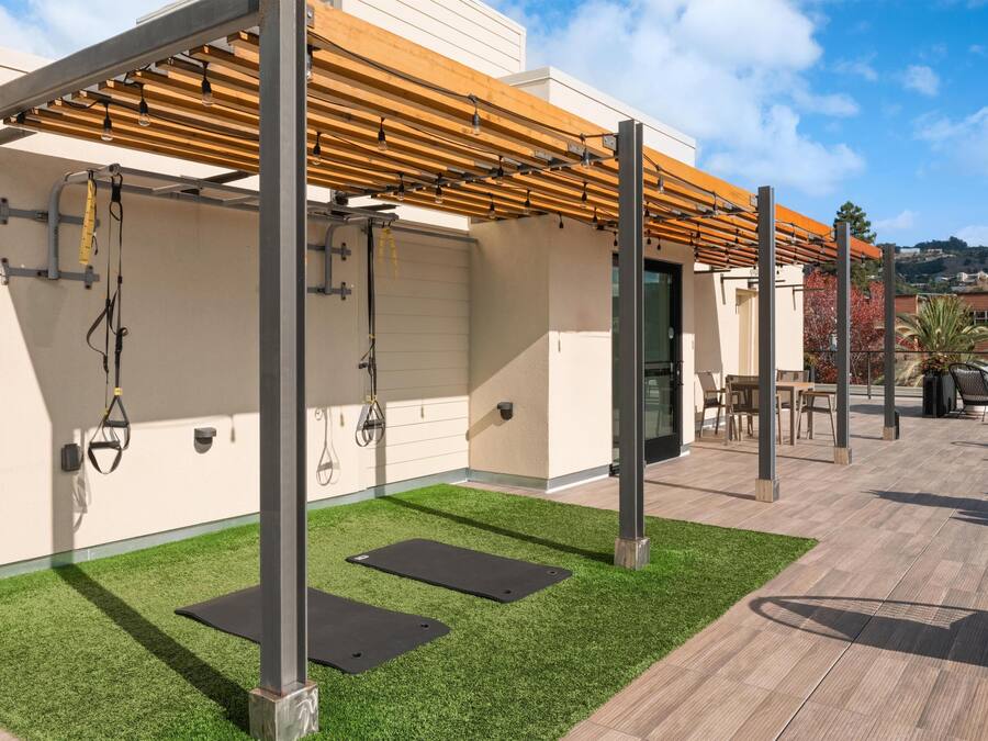 An outdoor workout area with exercise equipment, artificial grass, and a pergola structure.