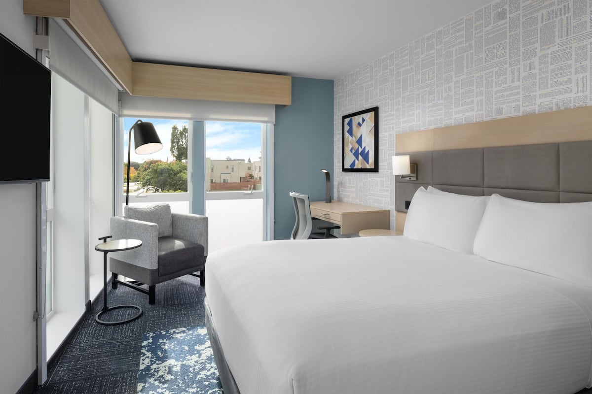 A hotel room with a large bed, a desk, a chair, and a TV.