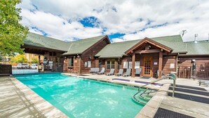 A pool area with a clear blue pool, wooden cabins, and lounge chairs.