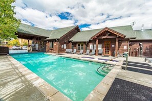Un área de piscina con una piscina azul cristalina, cabañas de madera y sillas de descanso.