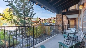 A balcony with outdoor seating, a stone wall, and a view of a parking area and buildings.