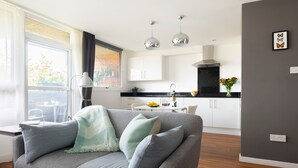 A modern living room with a grey sofa, a dining table, and a kitchen in the background. - Smart Modern Studio in Pimlico with Garden Views (London)