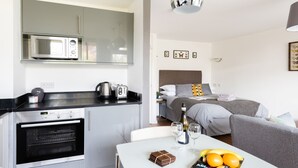 A compact kitchenette with a microwave, toaster, and coffee maker. A bed with a gray headboard and pillows is visible in the background. - Smart Modern Studio in Pimlico with Garden Views (London)