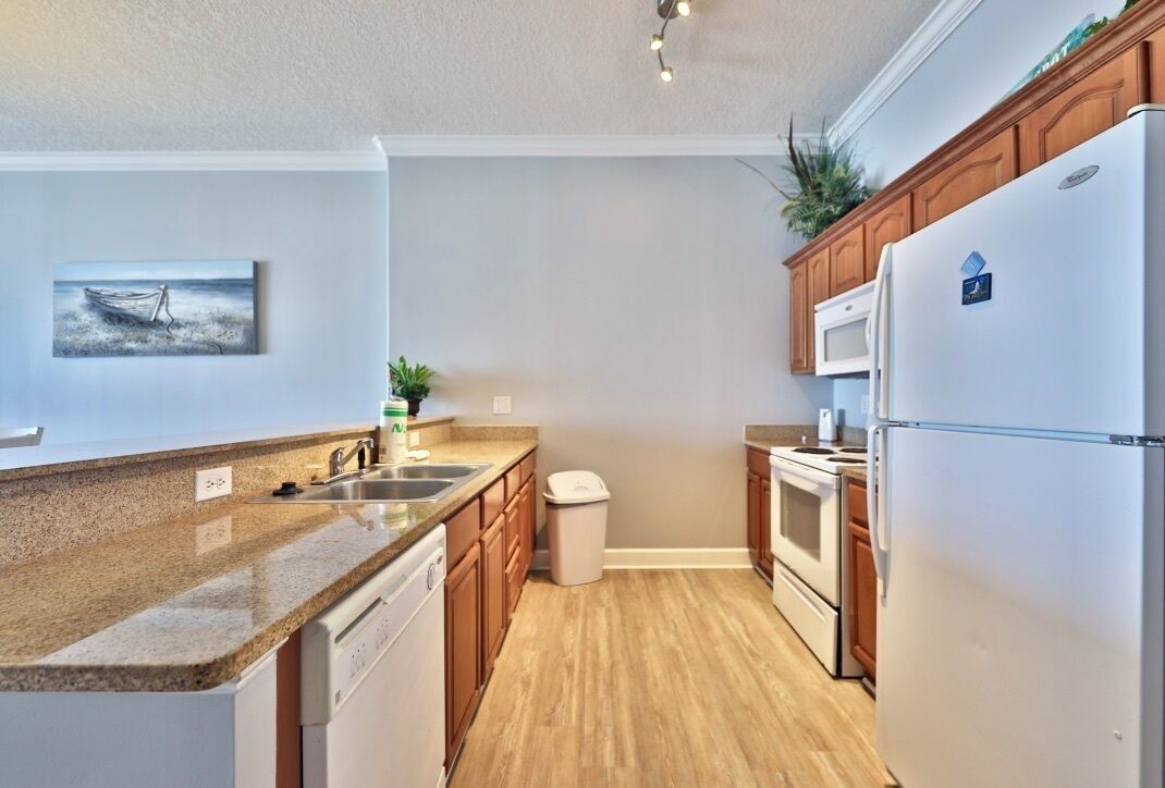 A modern kitchen with granite countertops, wooden cabinets, a stainless steel sink, a dishwasher, a refrigerator, and a microwave.
