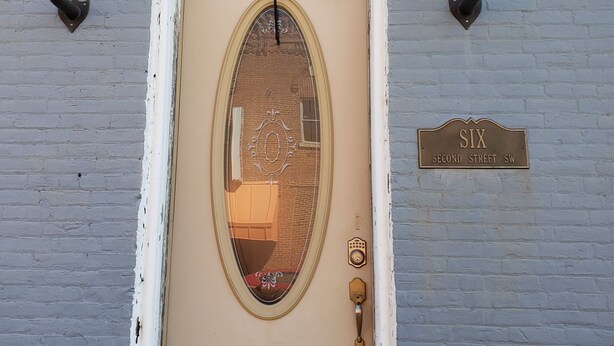 Een beige deur met een rondboogvenster, een messing deuropener en een bordje met de tekst 'SIX Second Street SW'.