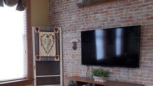Een woonkamer met een bakstenen muur, een flatscreen televisie die erop bevestigd is, een houten entertainmentkast eronder, en een raam met gordijnen.
