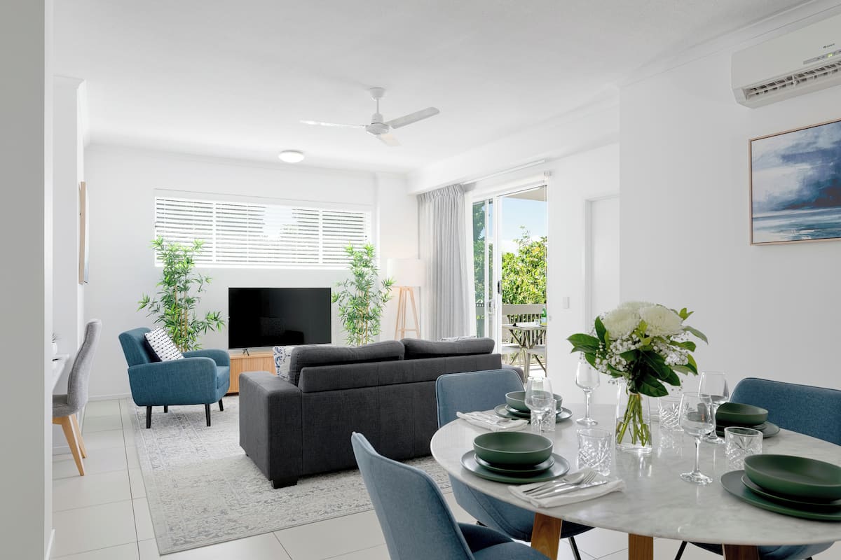 A modern living room with a sofa, TV, and dining area with a table set for two.