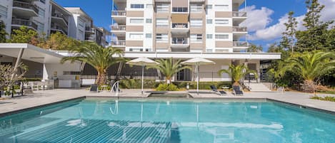 Una piscina al aire libre, sombrillas, sillones reclinables de piscina