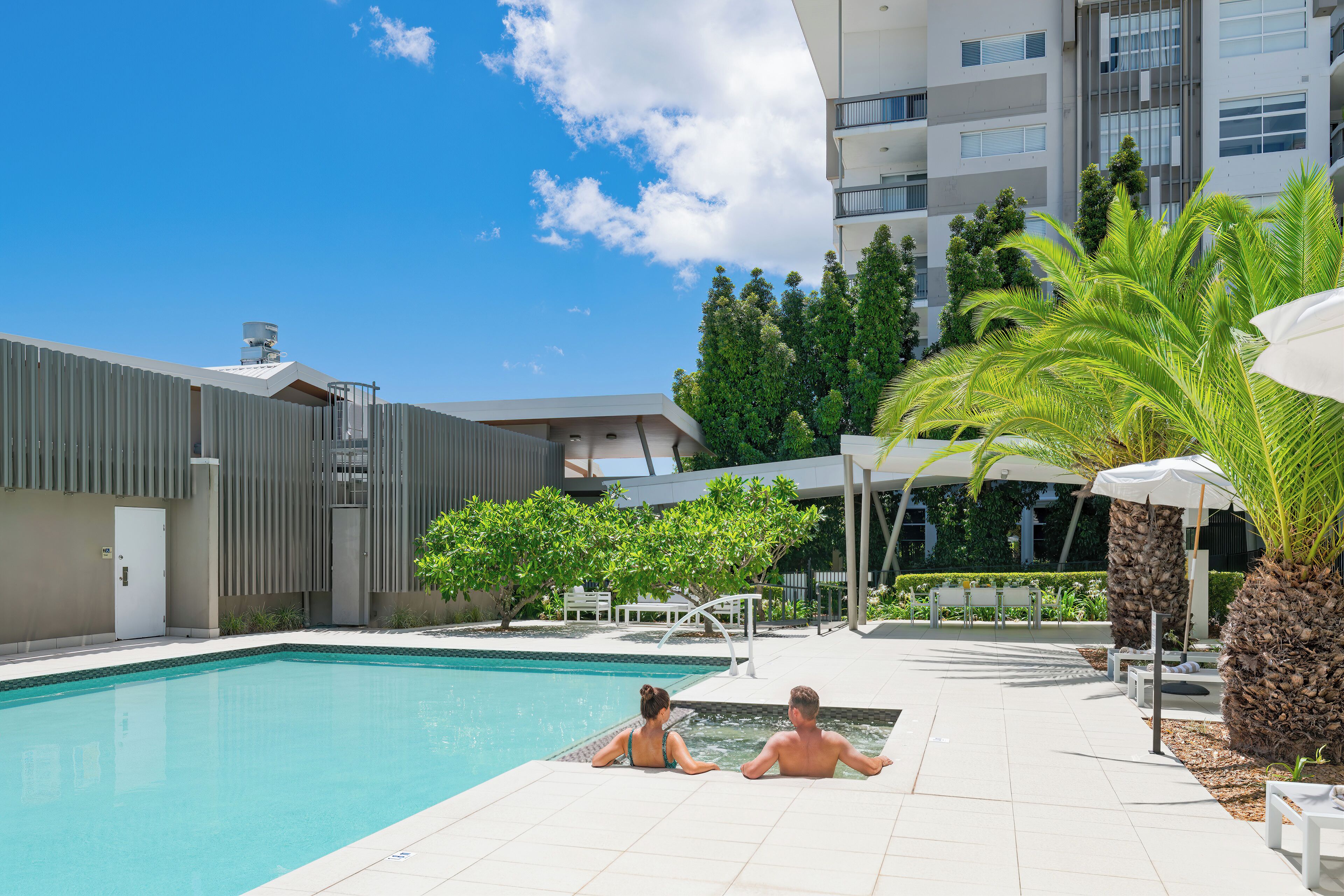 A swimming pool with two people, a modern building, and a clear sky.