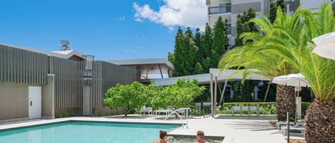 A swimming pool with two people, a modern building, and a clear sky.