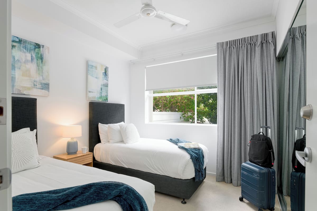 A hotel room with two beds, a window with curtains, a ceiling fan, and a suitcase.
