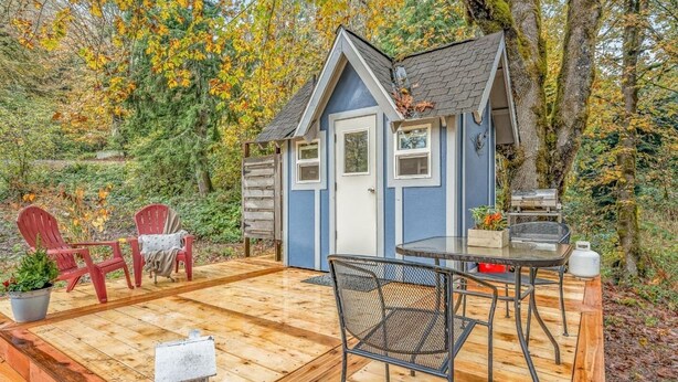 A small blue shed with a sloped roof, a wooden deck, a metal table, and two red Adirondack chairs. - Escape. Just You. Peace, Animals & Nature (Longview)