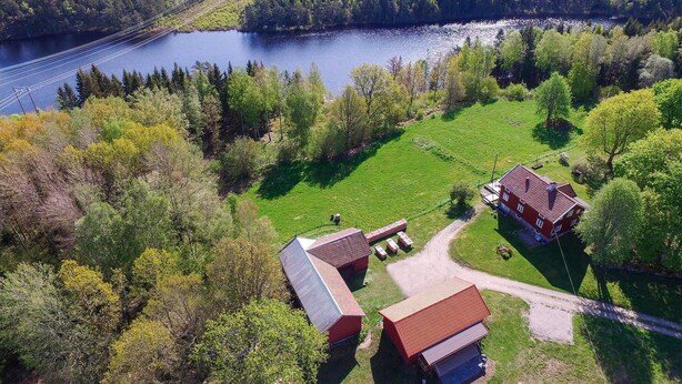 A rural property with a large body of water, a red barn, and a house with a sloped roof.
