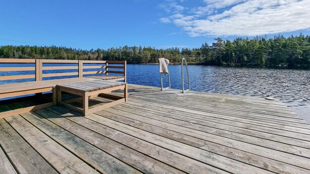 Un muelle de madera con un banco y un perchero, con vistas a un lago tranquilo rodeado de árboles.