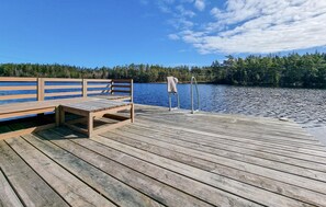 Une jetée en bois, agrémentée d’un banc et d’un porte-serviettes, d’où l’on peut admirer un lac paisible entouré d’arbres.