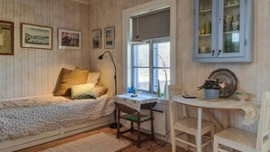 Un dormitorio acogedor con cama, escritorio y silla. Hay cuadros en la pared, una ventana con vistas y un aparador con puertas de cristal.