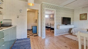 Una habitación acogedora con piso de madera, una cama, un televisor montado en la pared y una kitchenette con pileta y alacenas.