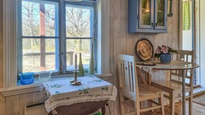 Una habitación rústica con una mesa y sillas de madera, una ventana con vistas a árboles, y un armario con una lámpara.