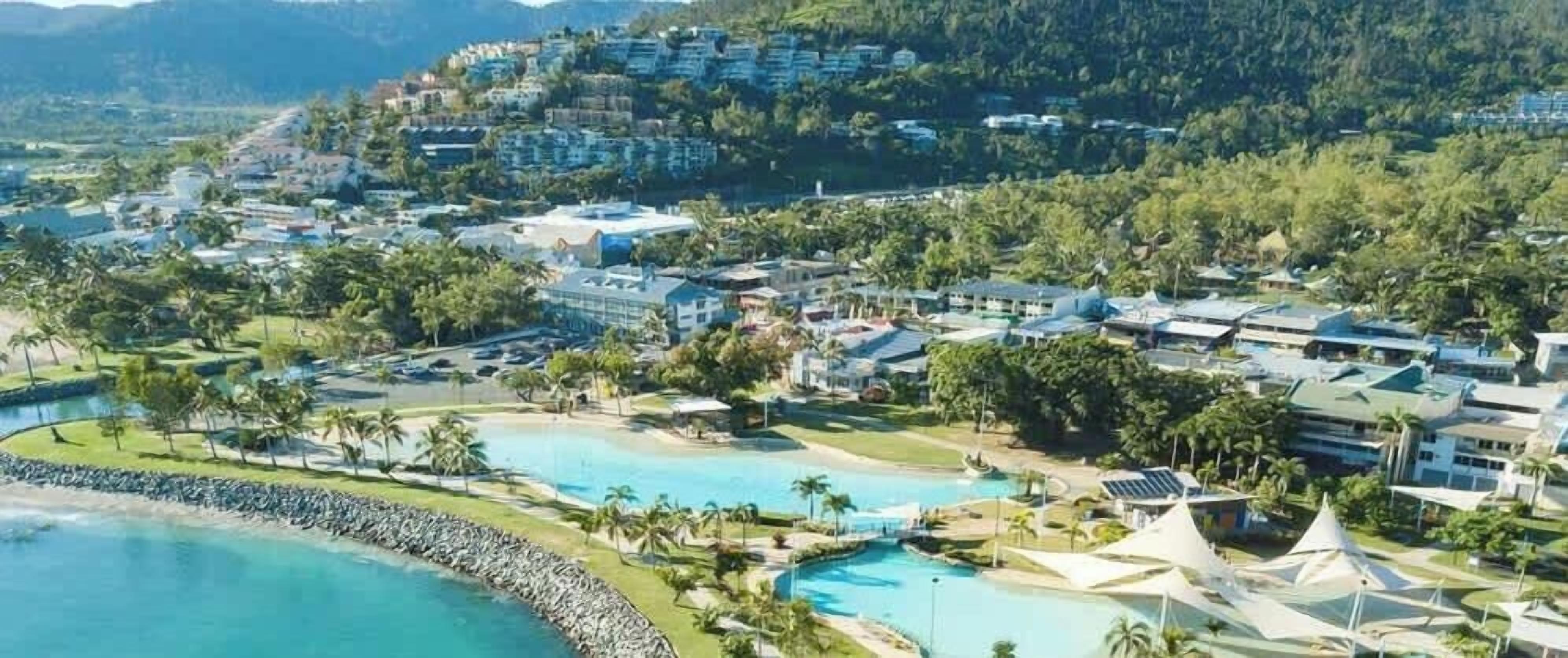 A resort with multiple swimming pools, a beach area, and a mountainous backdrop.