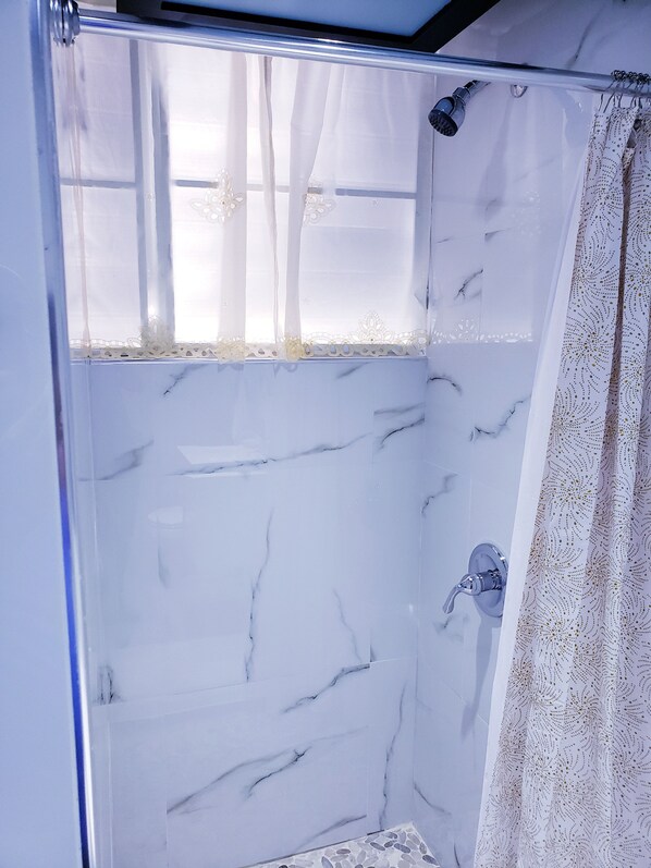 Une salle de bain avec une douche, une porte en verre et un rideau à motifs.