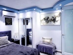 Une chambre à coucher comprenant un lit, des tables de chevet, une armoire et un grand tableau abstrait accroché au mur.