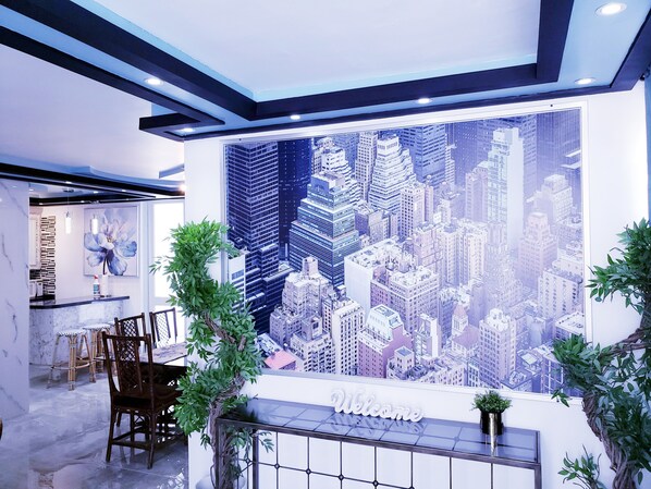 Un espace d’accueil agrémenté d’une fresque représentant un paysage urbain, d’une pancarte « Bienvenue » et d’un coin salon avec des chaises et une table.