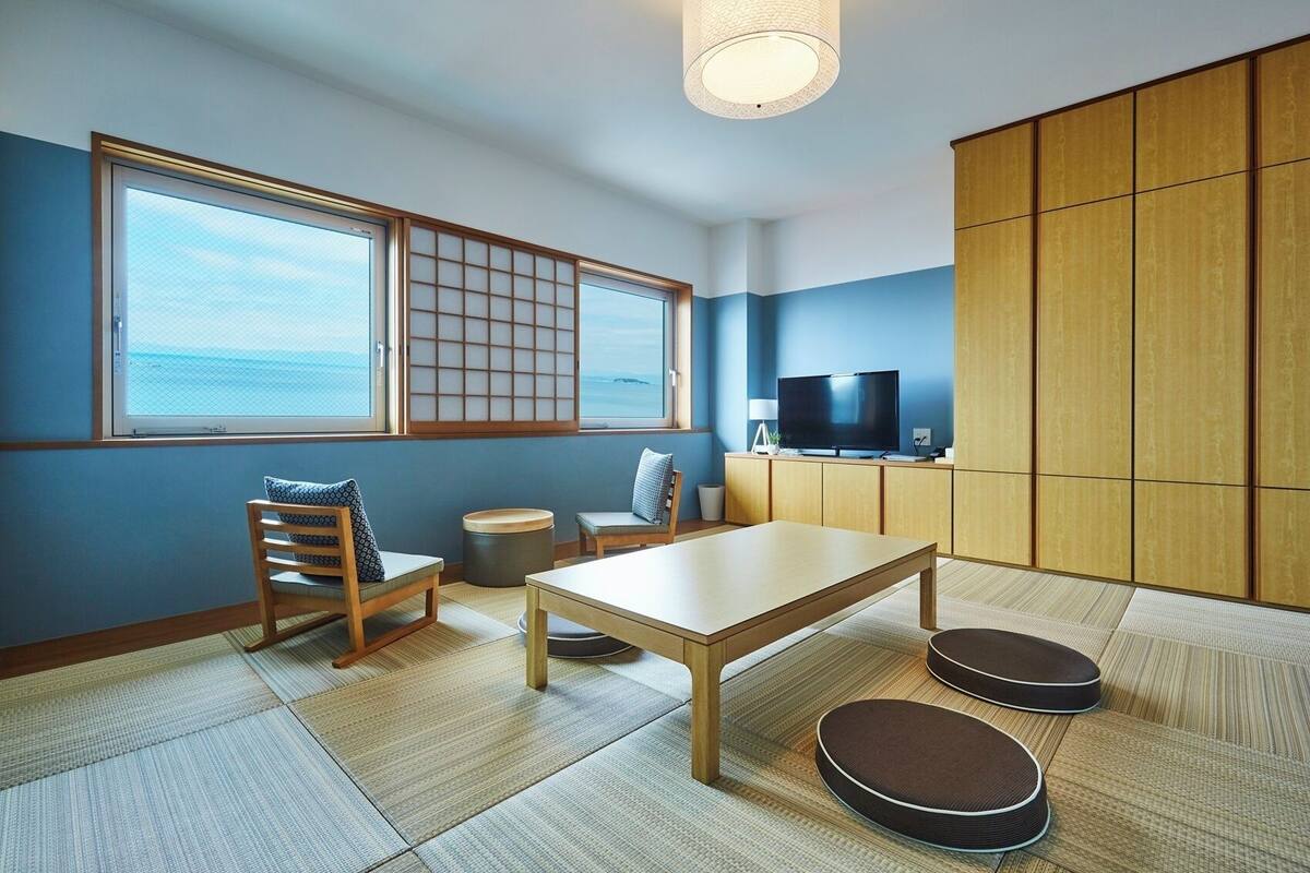 A room with tatami mats, a low table, a TV, and a view of the sea.