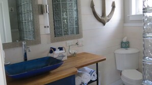Une salle de bain avec un lavabo bleu, un meuble-lavabo en bois, un récipient en verre, un porte-serviettes et des toilettes.