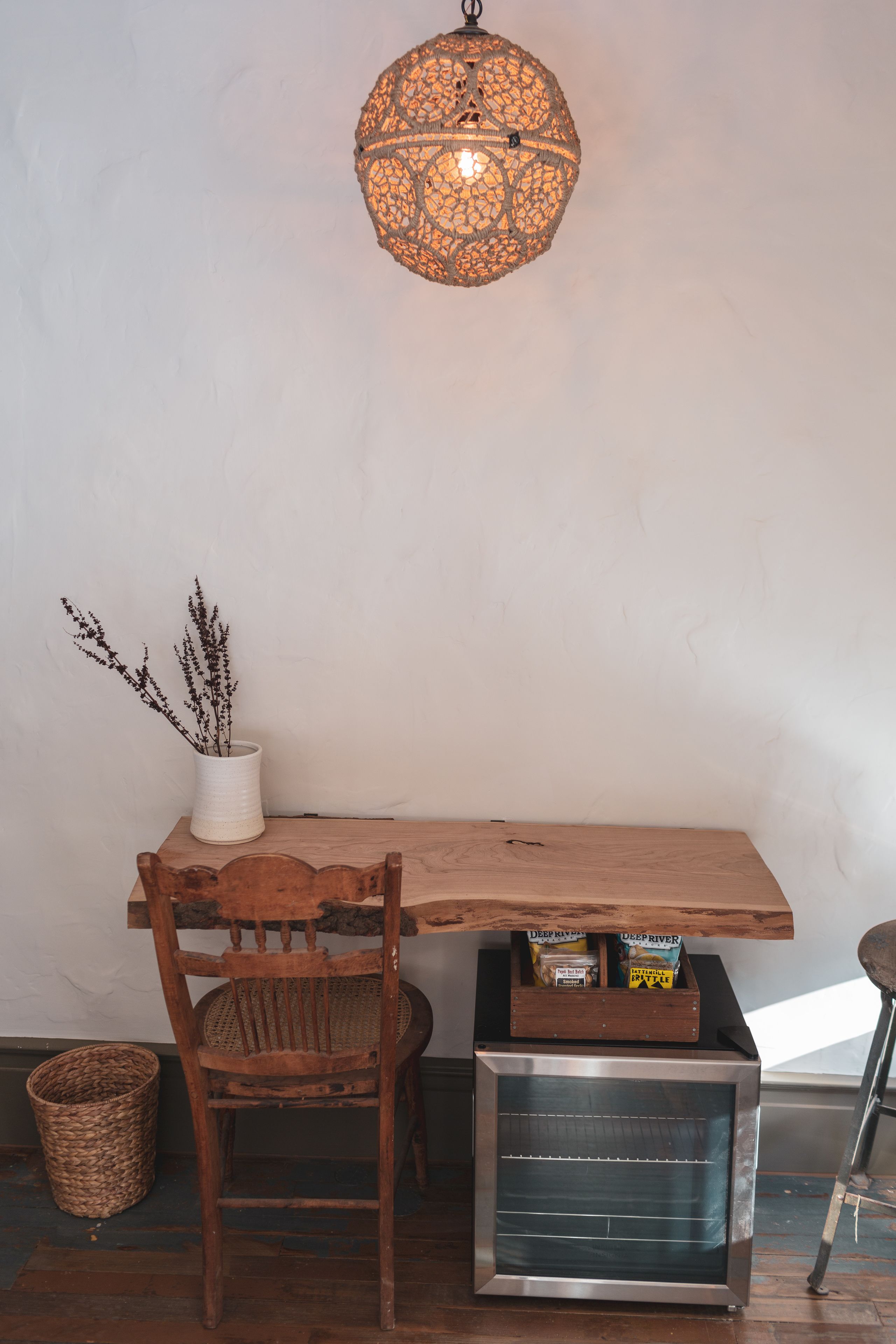 A wooden table with a white vase and dried plants, a wicker basket, and a vintage-style oven under a decorative hanging light fixture.