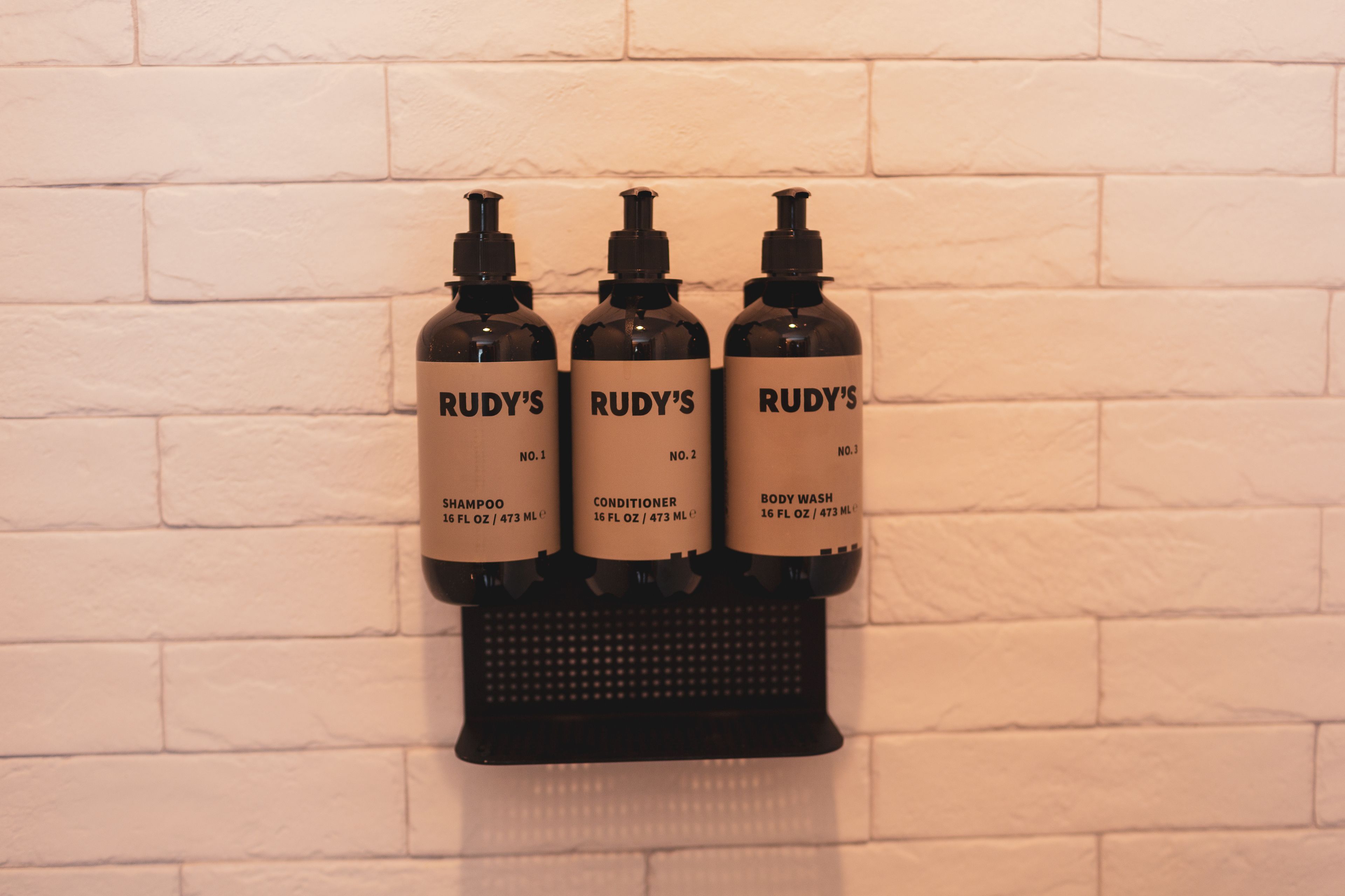 Three bottles of Rudy's products on a wall-mounted dispenser.