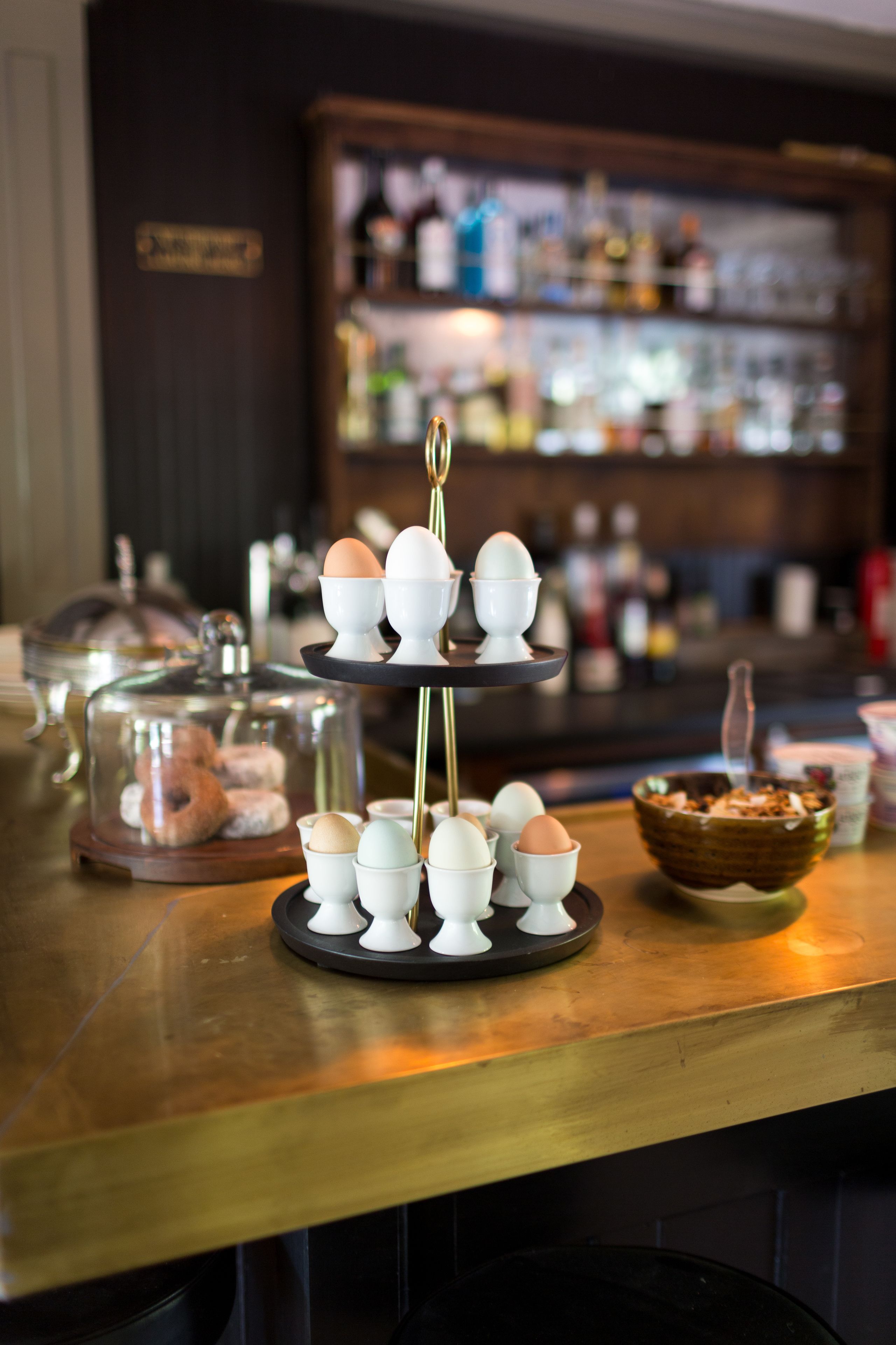 A three-tiered stand with eggs and a basket of pastries on a bar counter.