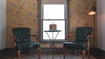 A room with two green leather chairs, a small table with a tissue box, and a window with floral wallpaper.