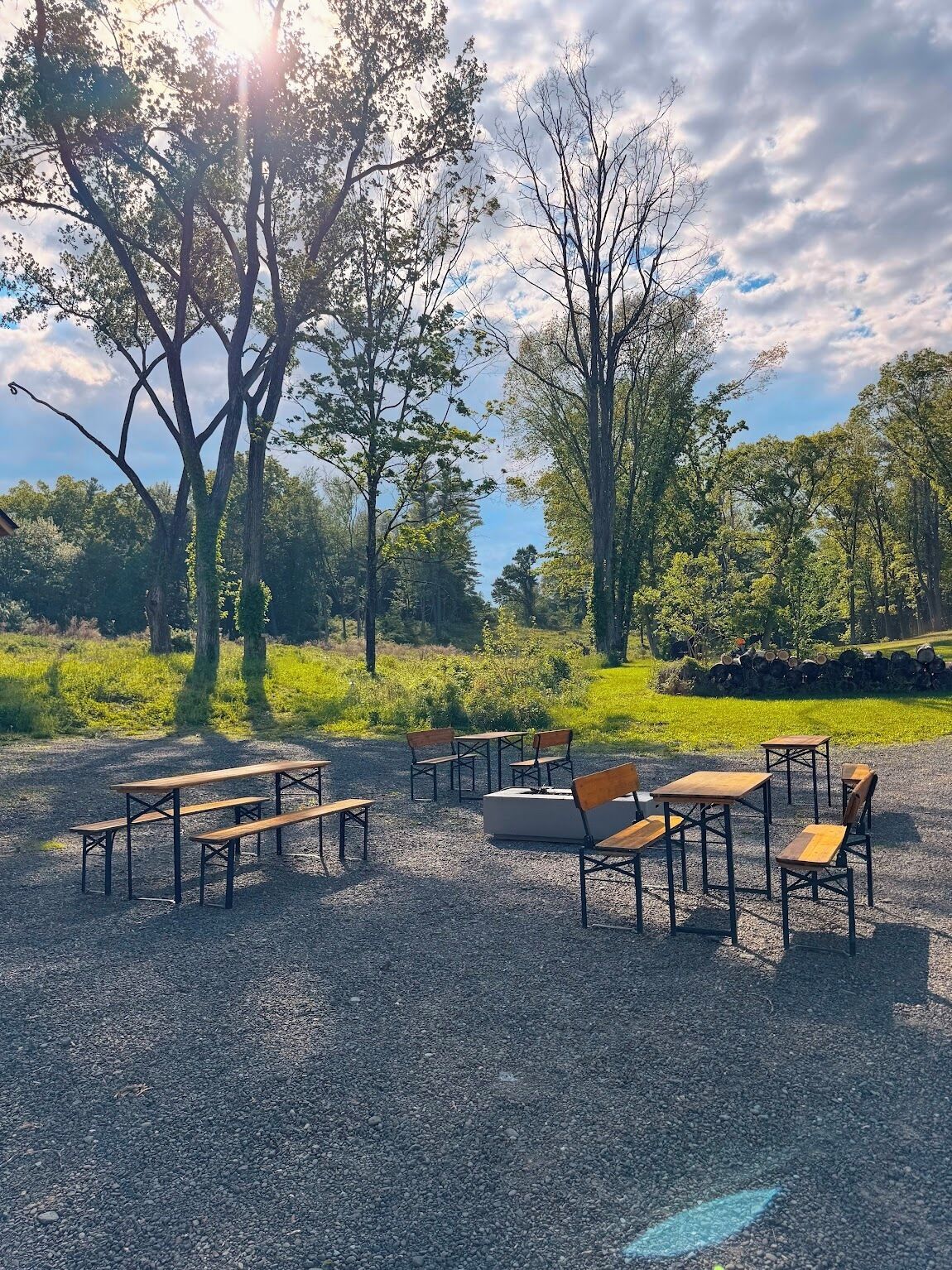 An outdoor seating area with tables and benches, surrounded by trees and greenery.