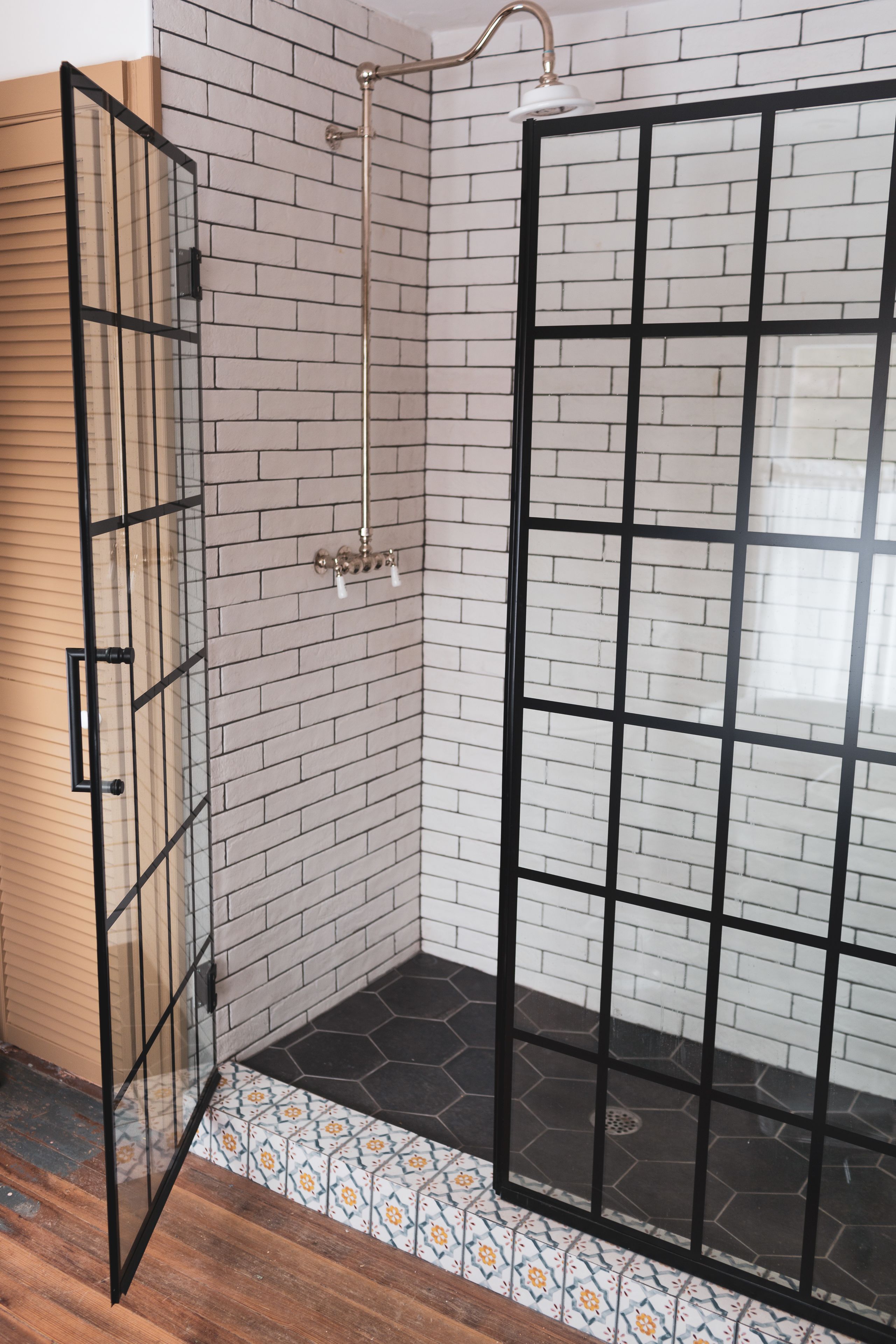 A shower area with a glass door, tiled walls, and a patterned floor.