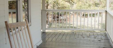 A covered porch with a ceiling fan, wooden chairs, and a view of trees.