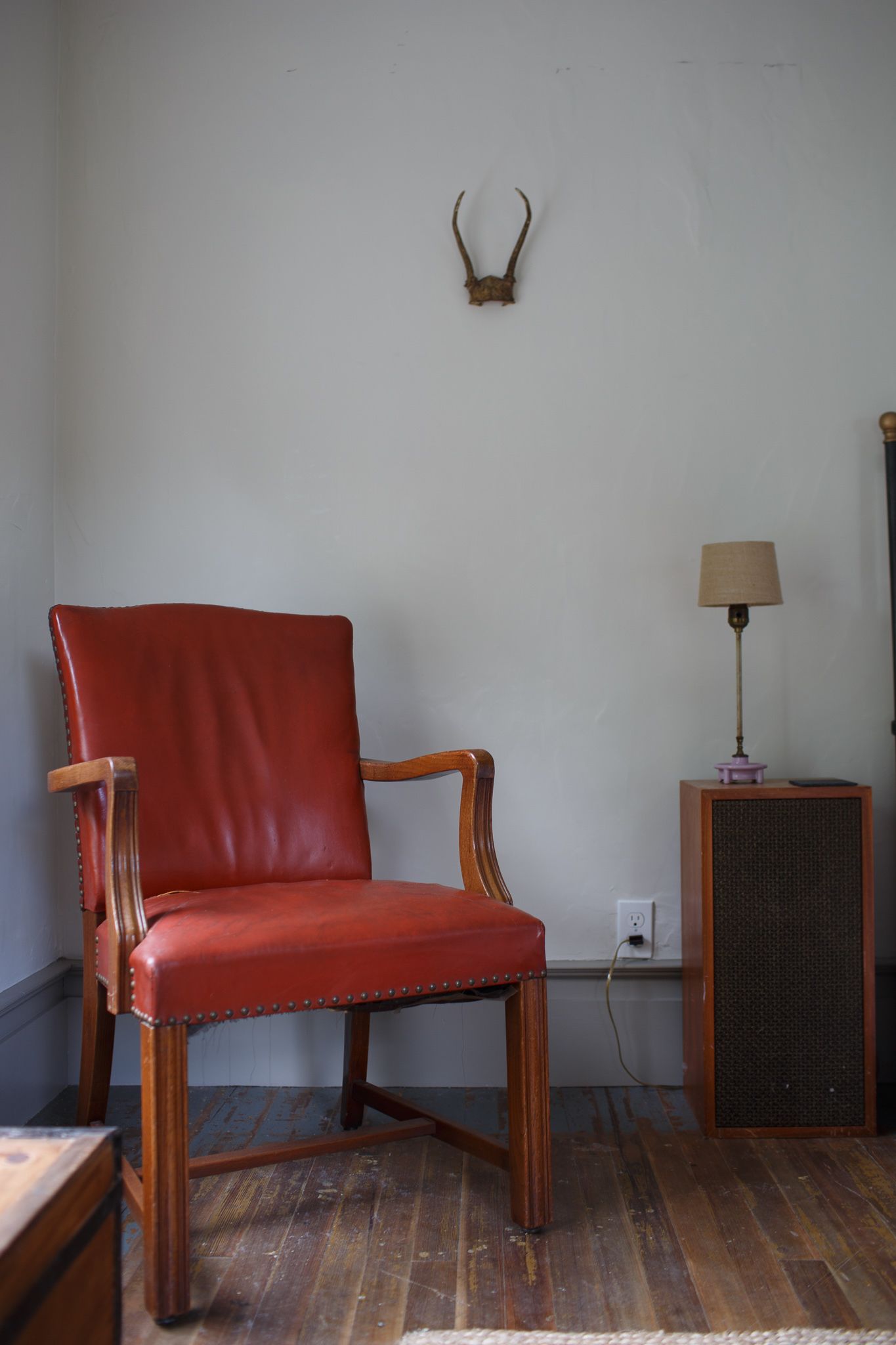 A red leather chair with wooden armrests and legs, a wall-mounted deer head, a lamp on a small table, and a speaker.