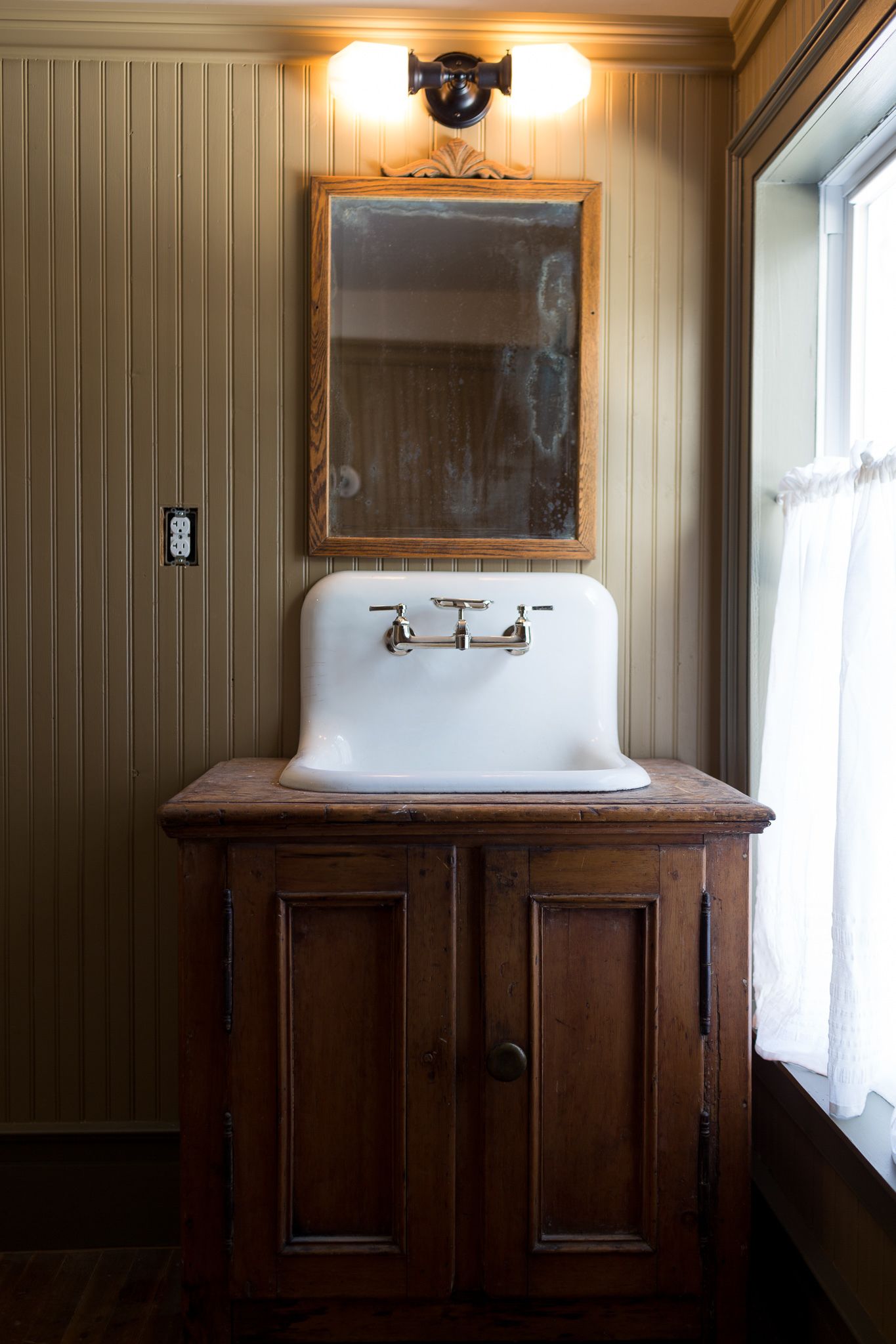 A bathroom with a wooden vanity, a white sink, and a mirror above it.