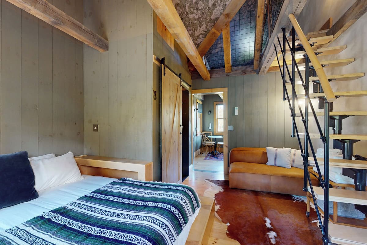A bedroom with a bed, a wooden ladder, and a cowhide rug.