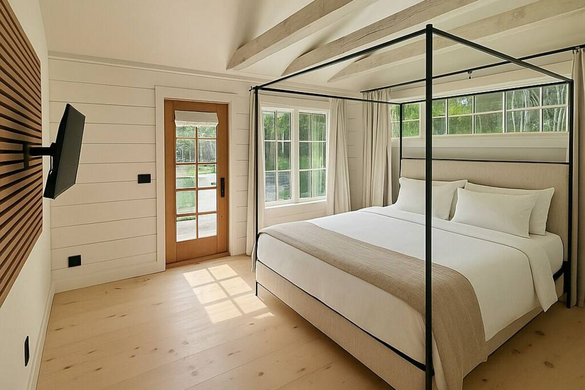 A bedroom with a four-poster bed, a television mounted on the wall, and a large window with curtains.