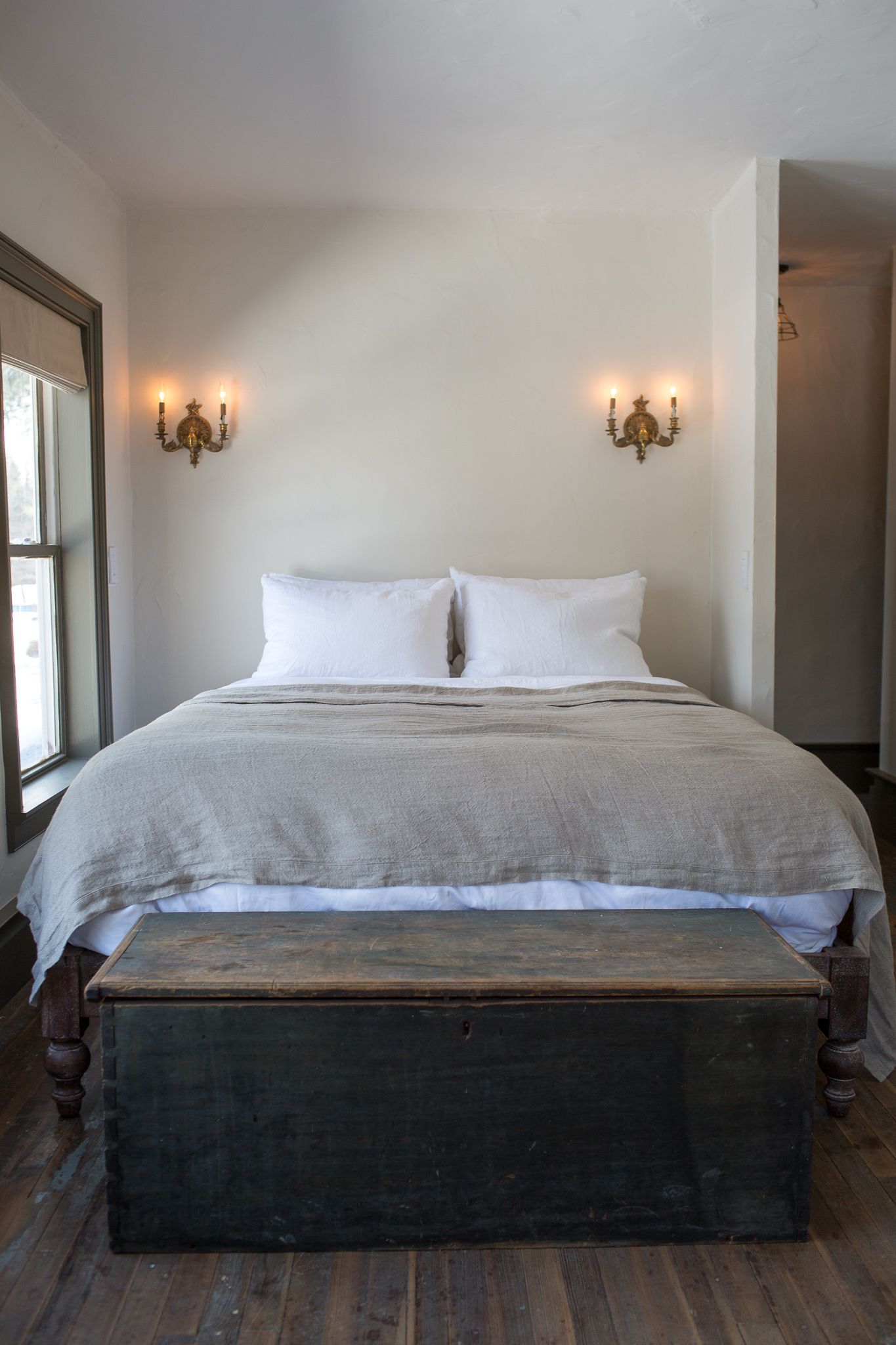 A bedroom with a large bed, two wall sconces, a wooden bench, and a window.