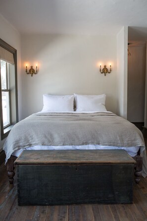 A bedroom with a large bed, two wall sconces, a wooden bench, and a window.