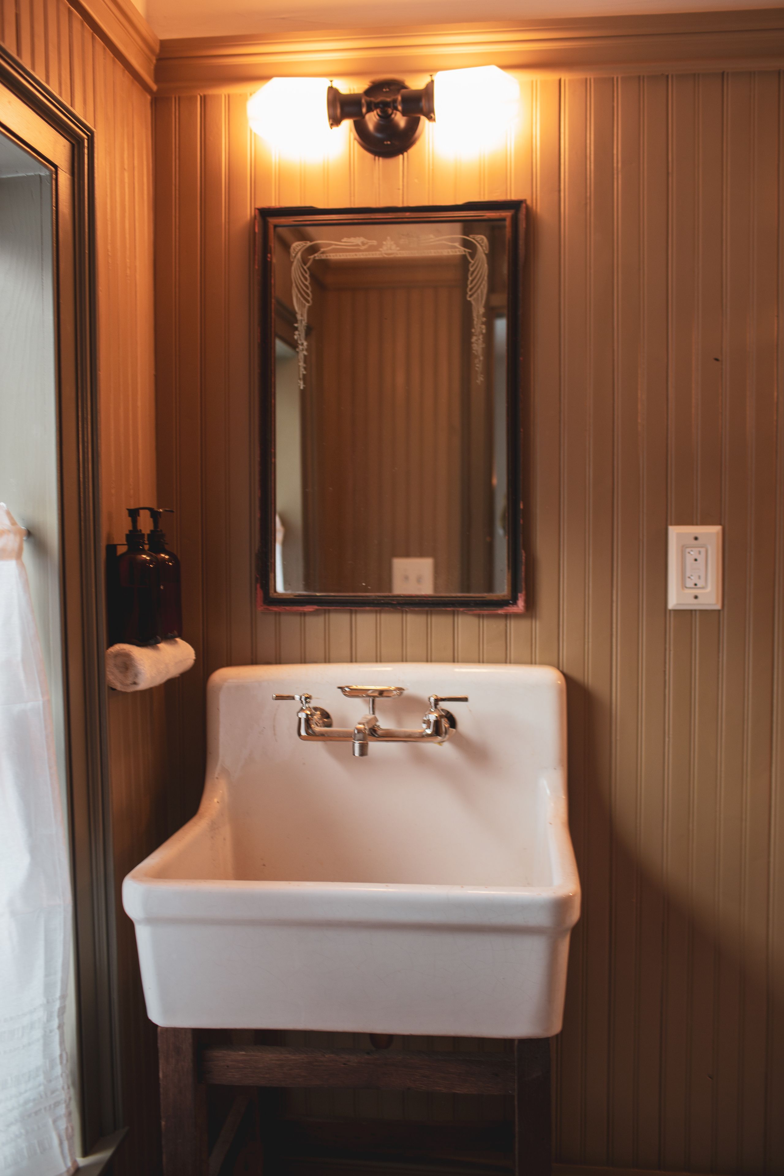 A bathroom with a white sink, wooden paneling, a mirror, and two bottles of hand soap on the wall.