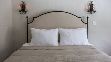 A bed with a headboard, two wall sconces, and a plain wall.