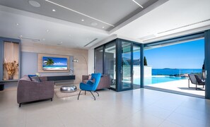 A modern living room with a large TV, comfortable seating, and a glass door leading to a pool with a scenic view. - Luxury Villa Elysian with Heated Pool (Mlini)