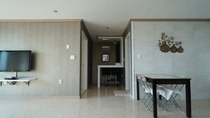A modern living room with a flat-screen TV, a dining table with chairs, and a hallway leading to a kitchen area. - Sunset in Garden (Seogwipo)