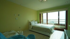 A bedroom with a bed, a chair, a small table, and a window with a view of the sea. - Sunset in Garden (Seogwipo)