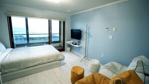 A hotel room with a bed, a TV, a window with a view, and a small seating area. - Sunset in Garden (Seogwipo)