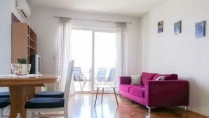 A living room with a wooden floor, a pink sofa, a dining table with chairs, a TV, and a sliding glass door leading to a balcony. - Apartment in Split with Seaview, Terrace, Air condition, WIFI (4749-1) (Split)